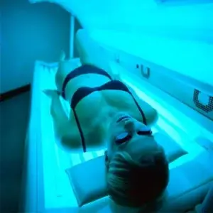 Mulher recebendo aplicação de bronzeamento artificial em goiânia em uma cabine, ilustrando a dúvida comum: bronzeamento na cabine faz mal?